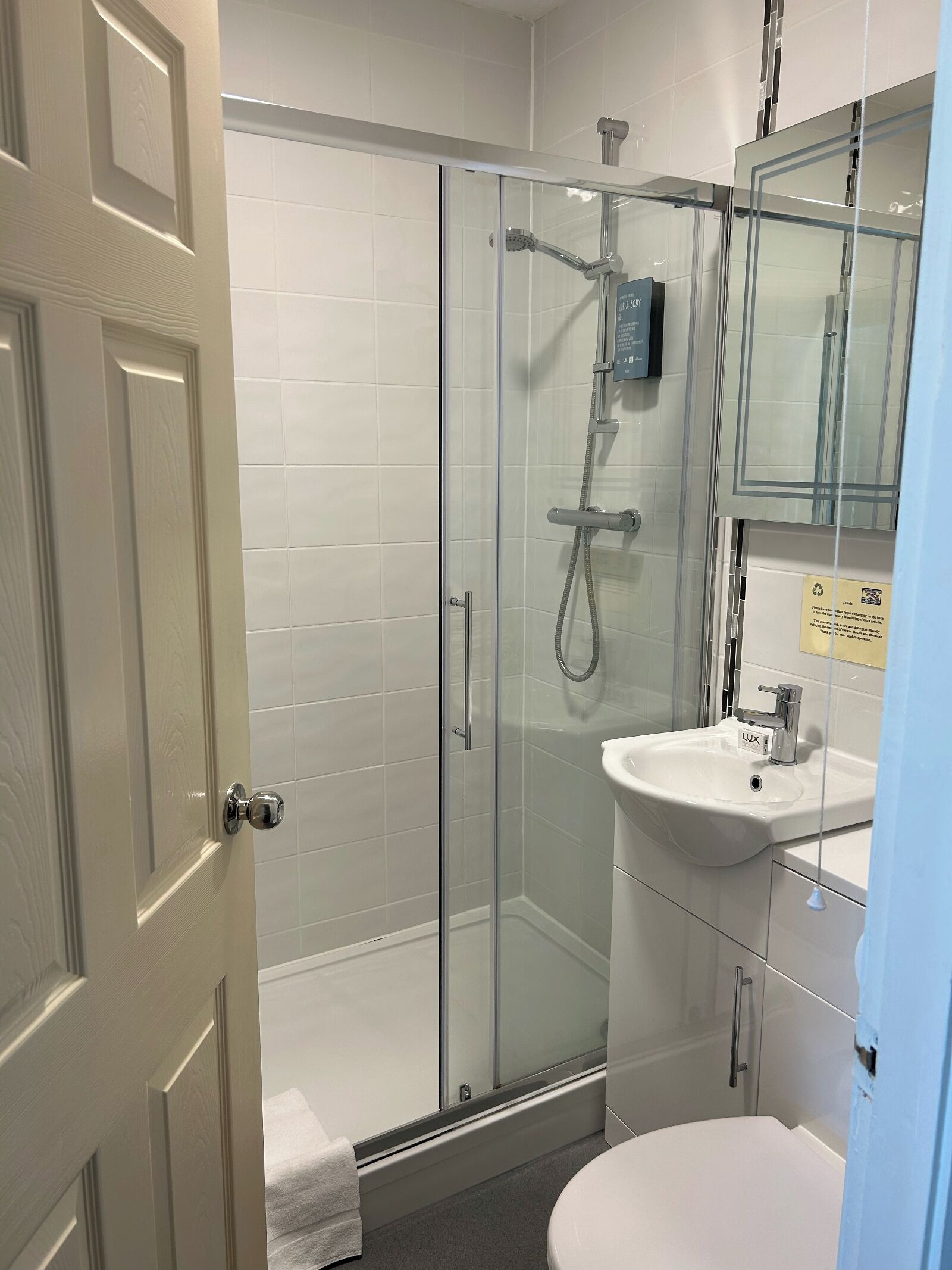A modern bathroom with a glass-enclosed shower, a white sink, and a large mirror.