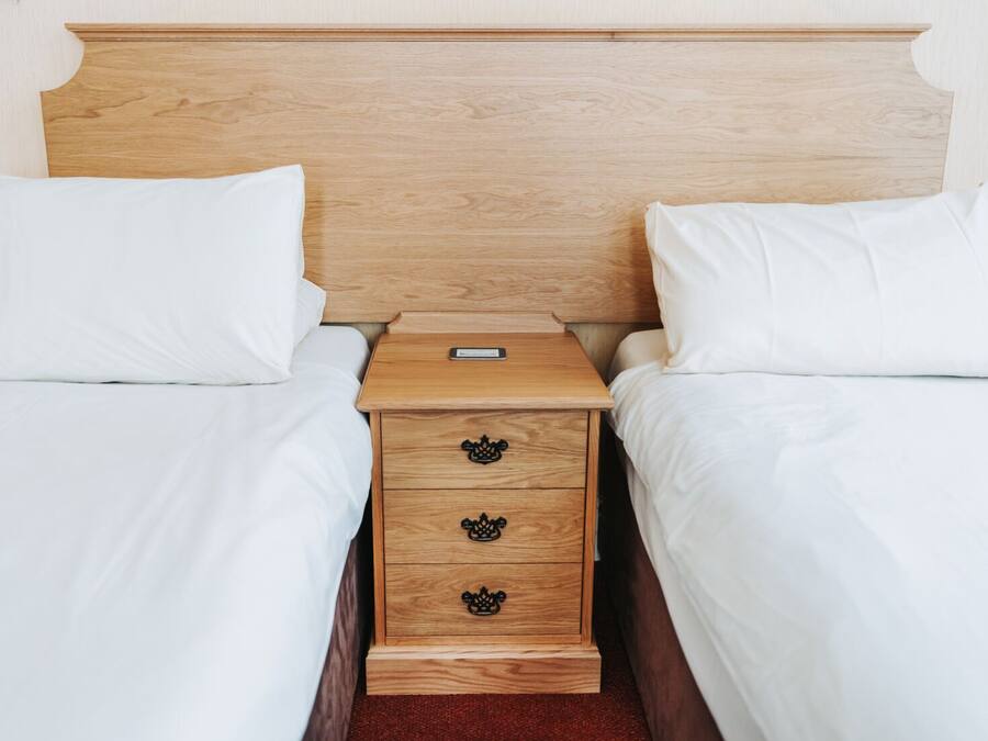 A hotel room with two single beds, a wooden headboard, a nightstand with drawers, and a small table.
