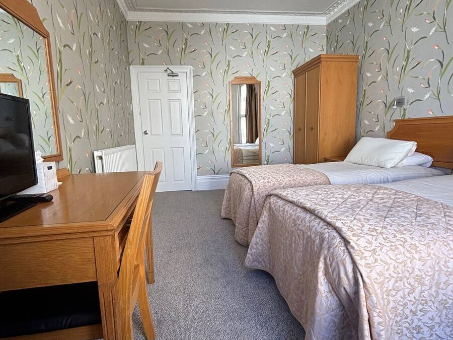 Quarto de hotel com duas camas, uma escrivaninha de madeira, uma televisão e um guarda-roupa.