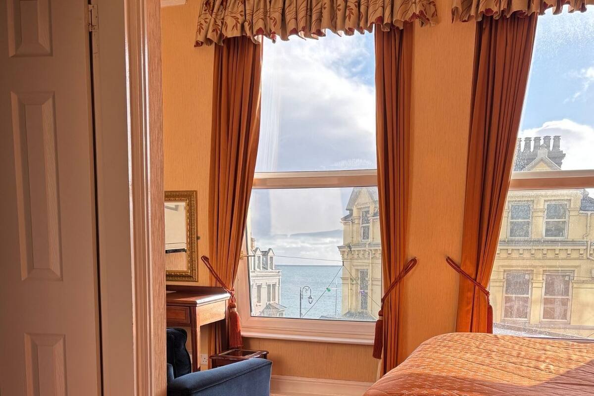Une chambre d’hôtel avec un lit, un bureau, une chaise et une vue sur les bâtiments par la fenêtre.