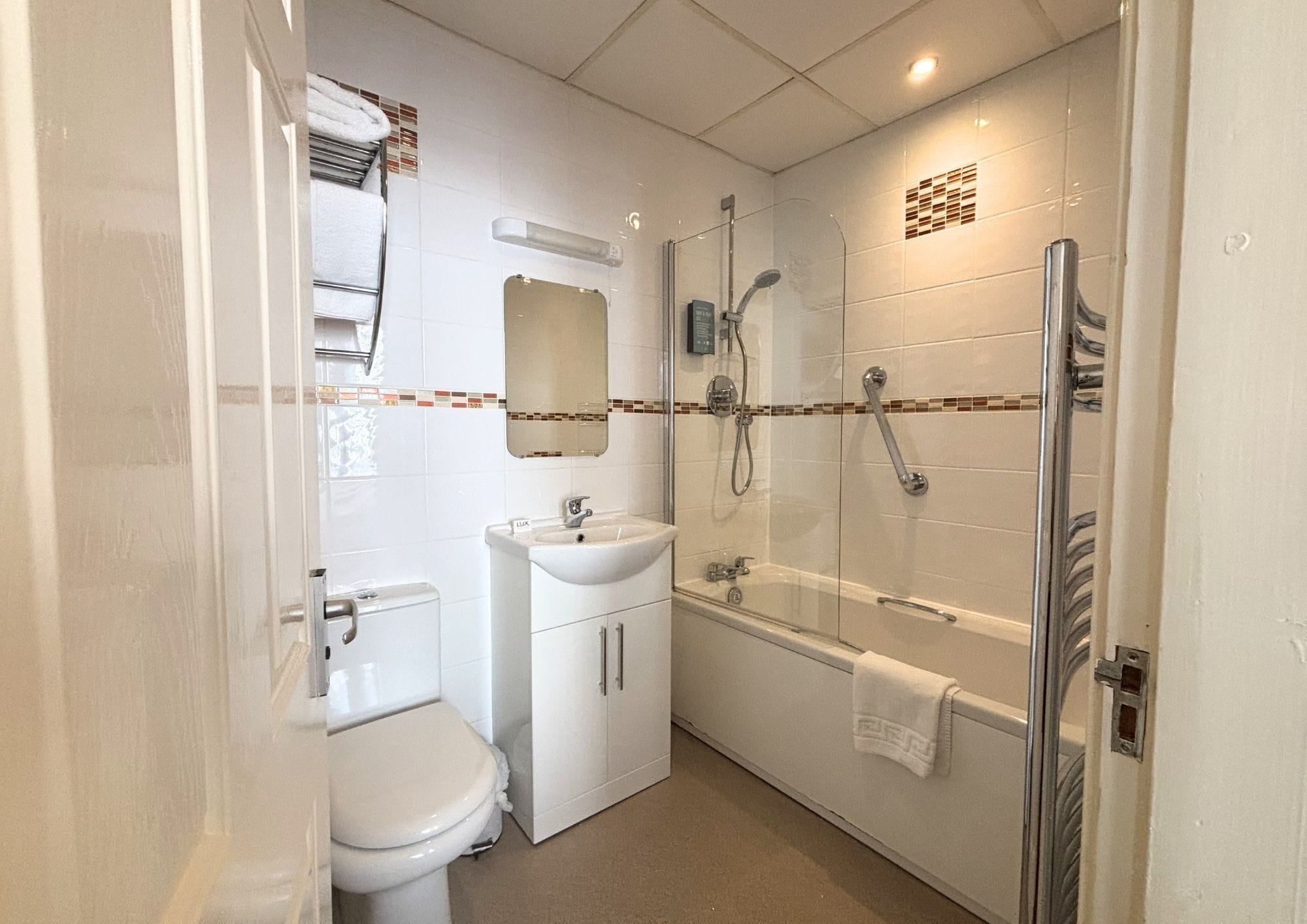 A compact bathroom with a toilet, sink, and glass-enclosed shower area.