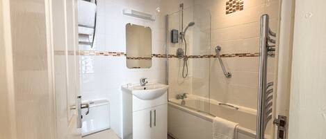 Un baño pequeño con inodoro, lavabo y cabina de ducha con mampara de vidrio.