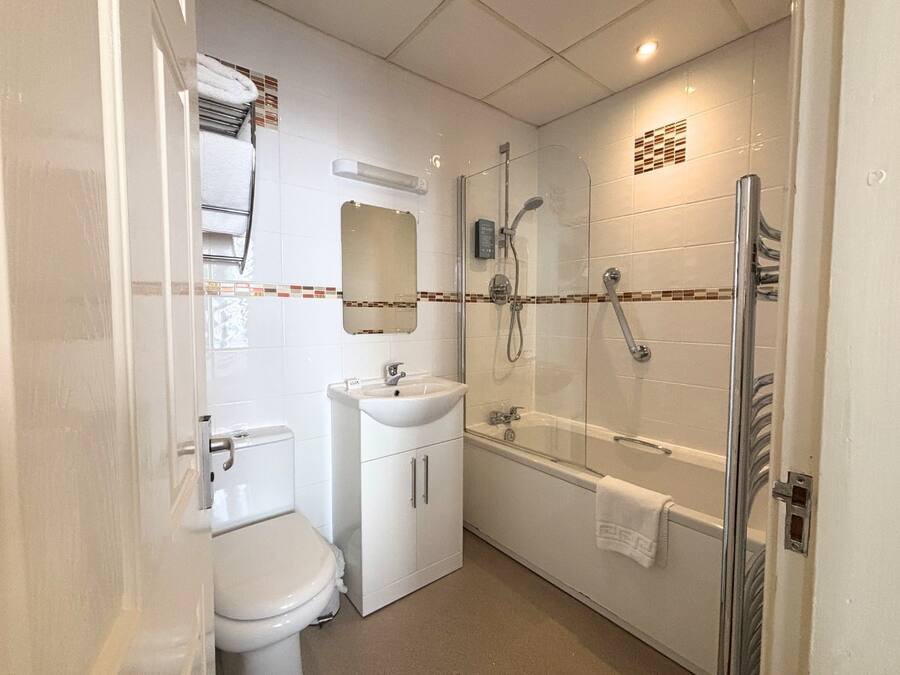 A compact bathroom with a toilet, sink, and glass-enclosed shower area.