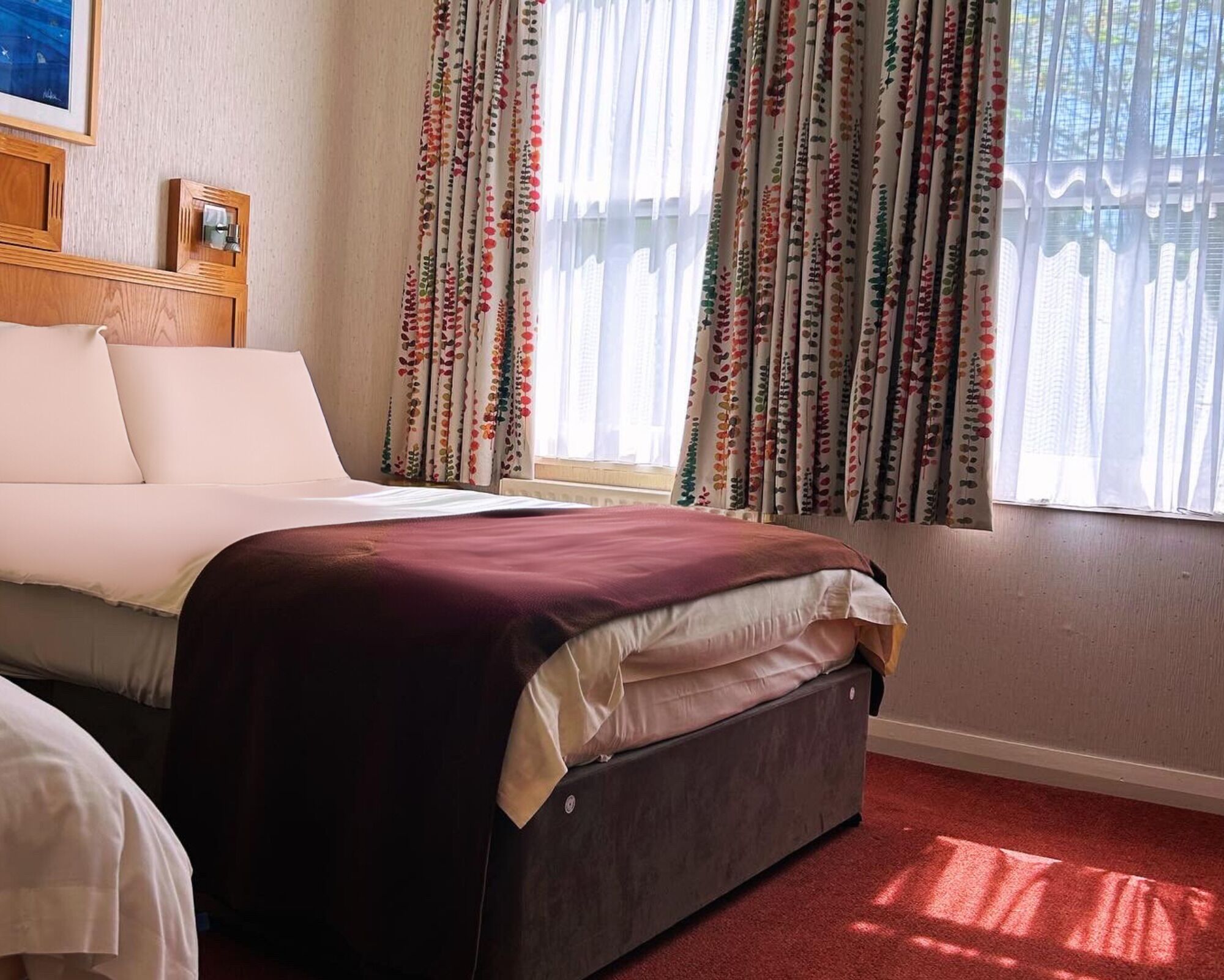 A hotel room with a bed, a bedside table, and curtains.