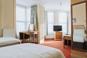 Habitación de hotel con dos camas, un escritorio con silla, un televisor y un espejo grande.