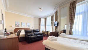 Een hotelkamer met een bed, een leren bank, een bureau, een stoel, een televisie en kunstwerken aan de muur.