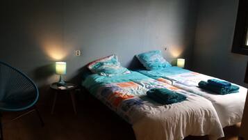 A room with two beds, each with a blue and white patterned duvet, a teal chair, and two bedside lamps.