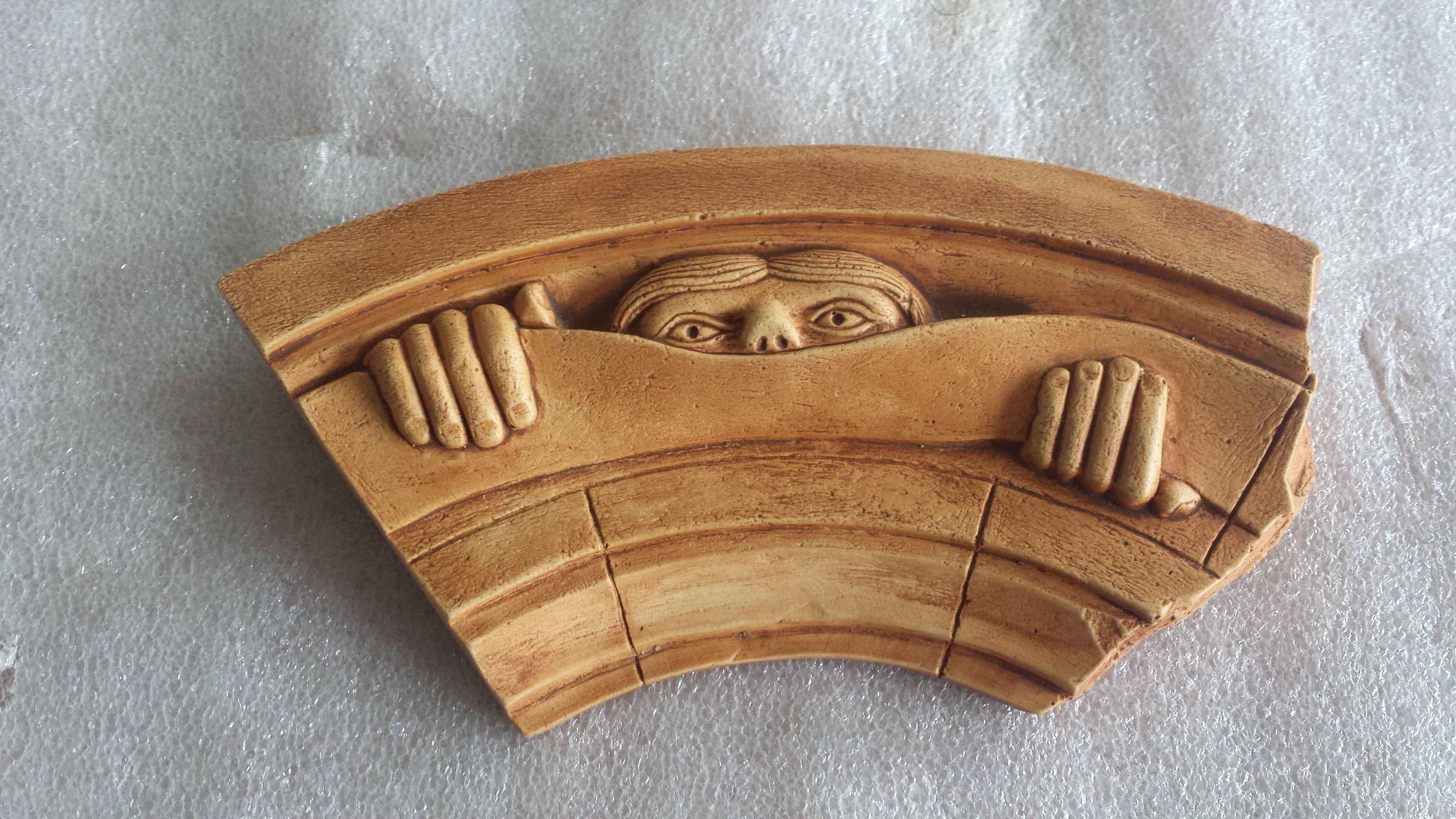 A wooden carving with a face peeking over a curved structure.