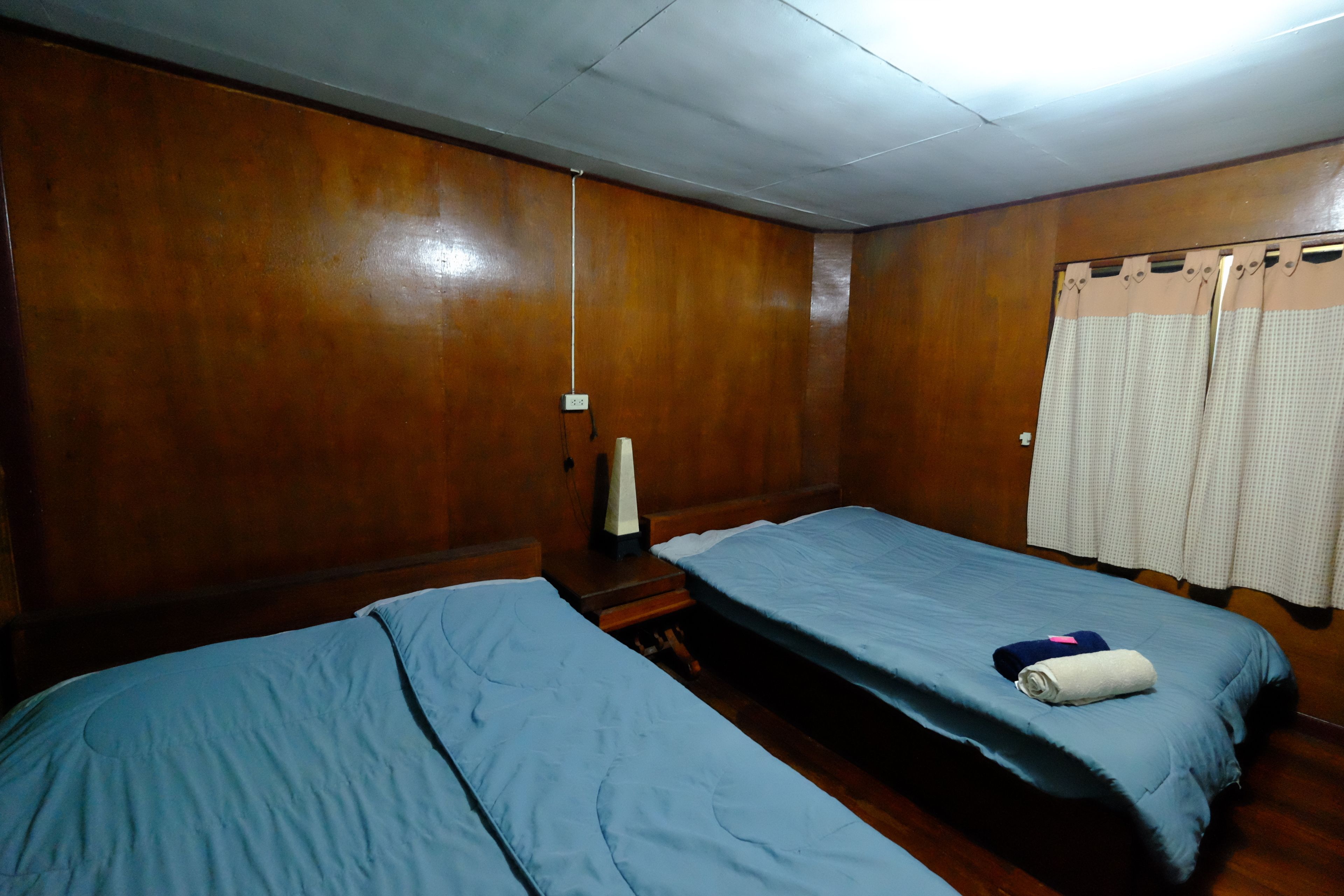 A room with two single beds, wooden walls, a small table, and a curtain.