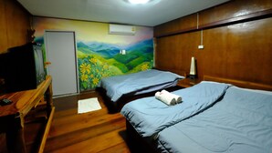 Una habitación con dos camas, piso de madera, un mural en la pared, un televisor y un escritorio.