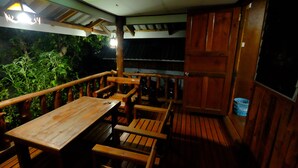 Una terraza de madera con una mesa y bancos, rodeada de follaje.