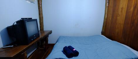 A small room with a bed, a wooden desk, a television, and a wall-mounted air conditioner.