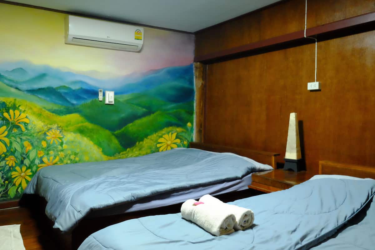 A room with two beds, a mural of a landscape, an air conditioner, and a wooden wall.