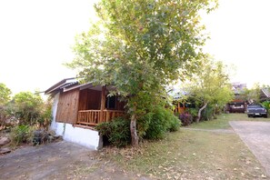Ett hus med en veranda av trä, omgivet av grönska och med en parkerad bil.