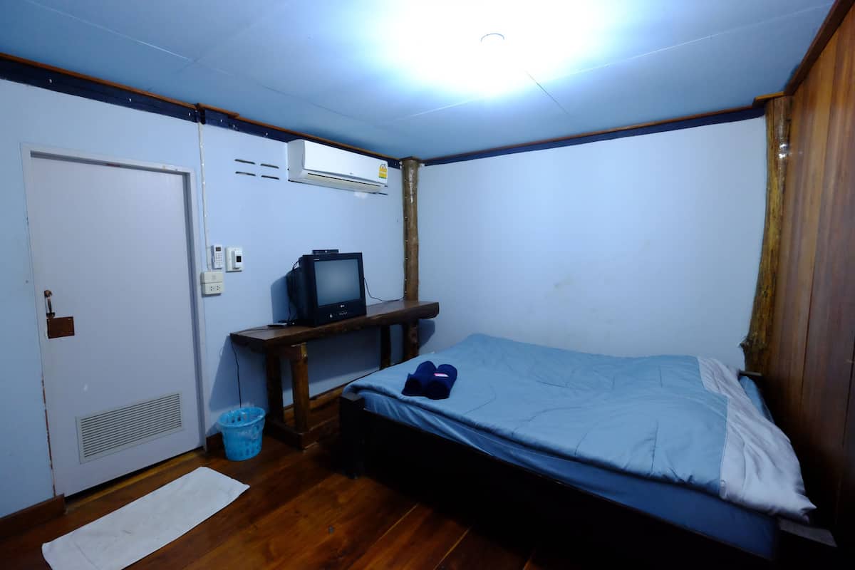 A small, compact room with a single bed, a desk with a computer, a door, and an air conditioning unit.
