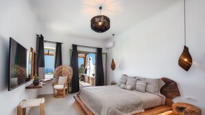 A bedroom with a large bed, a TV, a wooden stool, and a view of the outdoors. - Ayama Hideaway Villa by Calm Collection (Santorini)