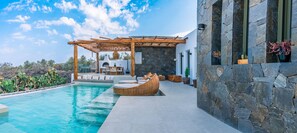 A modern outdoor pool area with a pergola, seating, and stone walls. - Ayama Hideaway Villa by Calm Collection (Santorini)