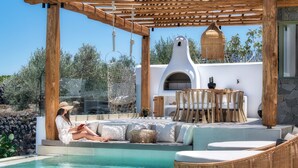A poolside area with a wooden pergola, outdoor seating, and a stone wall. - Ayama Hideaway Villa by Calm Collection (Santorini)