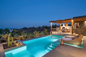 A swimming pool with a sunken seating area, a stone wall, and a view of the ocean. - Ayama Hideaway Villa by Calm Collection (Santorini)