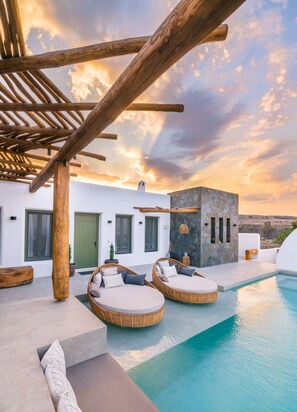 A modern outdoor pool area with wicker loungers and a stone wall. - Ayama Hideaway Villa by Calm Collection (Santorini)