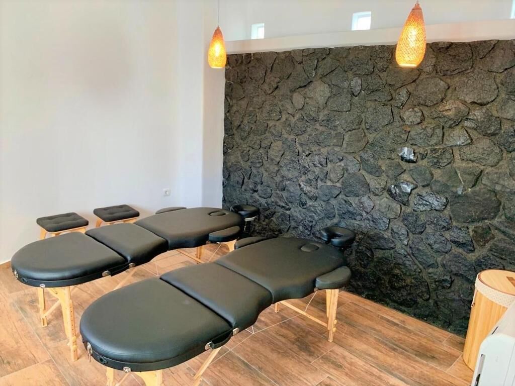 Ein Raum mit Steinwand und Holzboden, ausgestattet mit mehreren schwarzen Massagetischen und einer kleinen Holzeinrichtung.