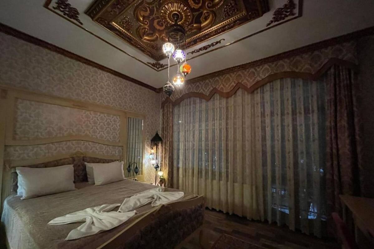 A hotel room with a large bed, ornate ceiling, and curtains.