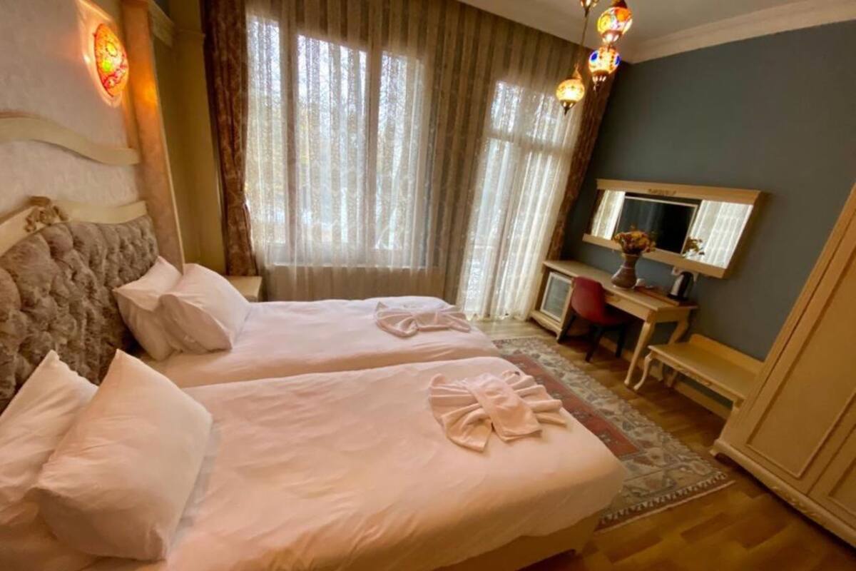 A hotel room with two beds, a desk, a chair, and a large window with curtains.