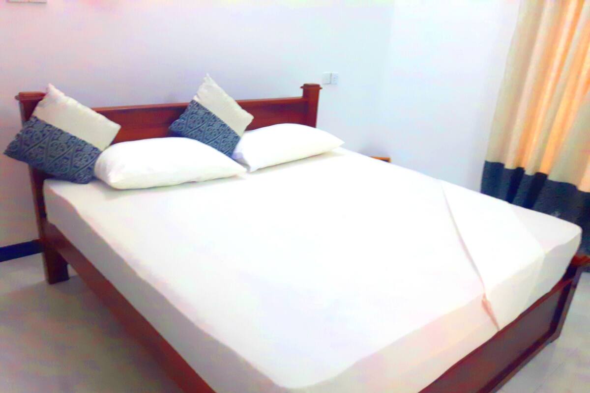 Cama bem arrumada, com estrutura de madeira, roupa de cama branca e dois travesseiros decorativos.