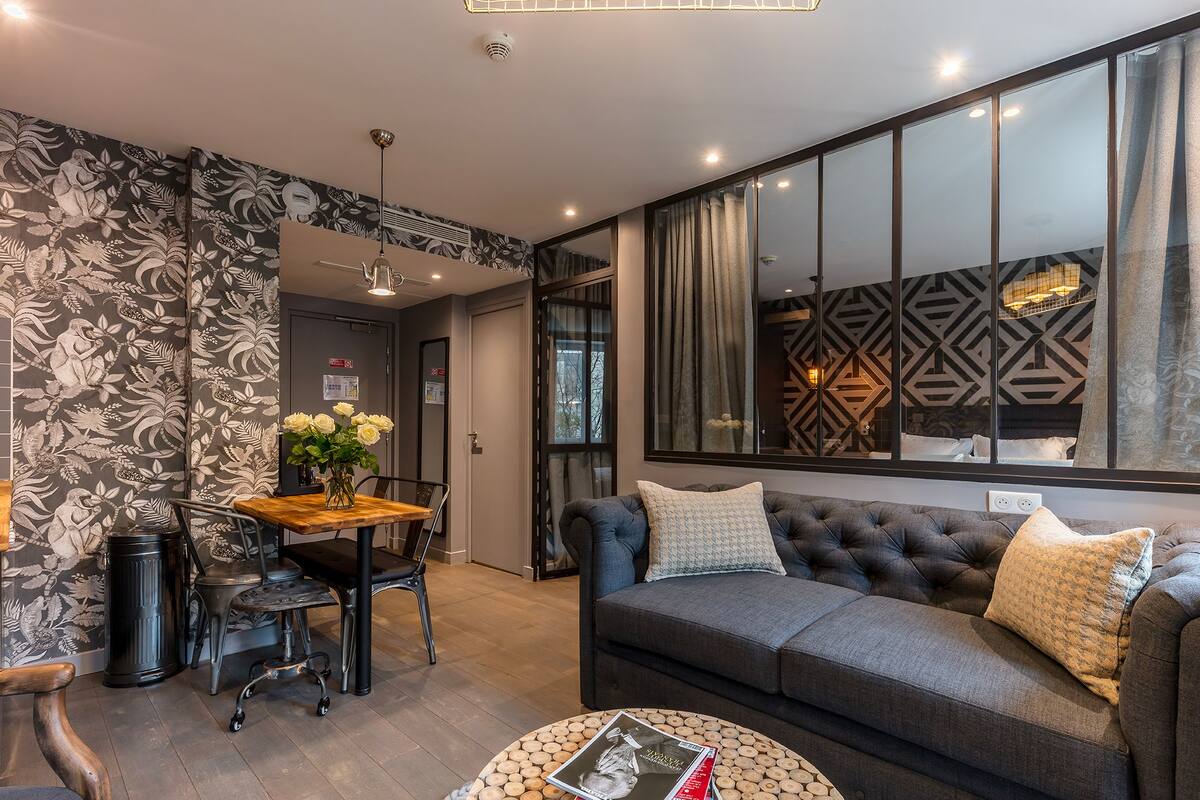 Ein modernes Wohnzimmer mit einem grauen Sofa, einem Holzesstisch und einer Wand mit Muster.