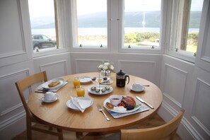 A breakfast table set with plates, cups, and a coffee pot, overlooking a scenic view.