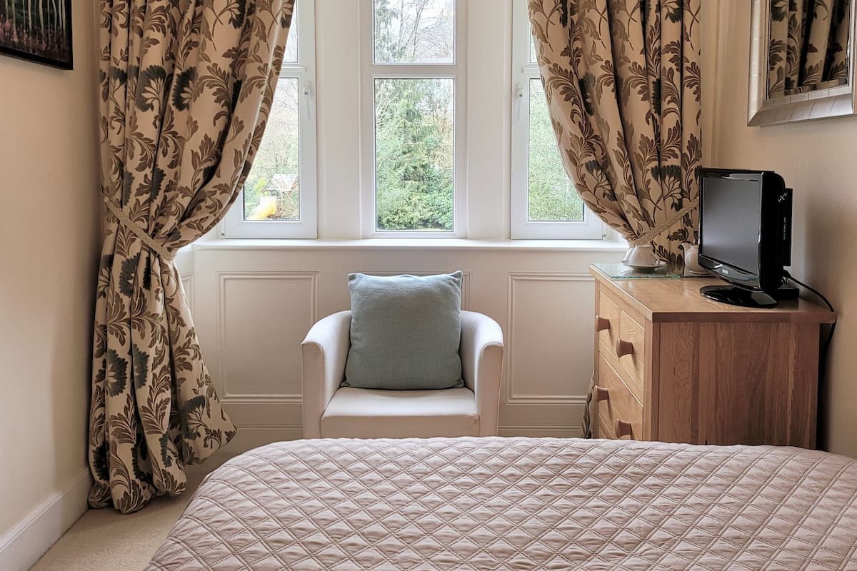 A bedroom with a bed, a chair, a desk with a computer, and curtains.