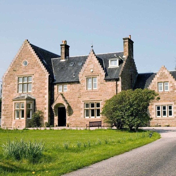 A large stone building with multiple chimneys, a central entrance, and a well-maintained lawn.
