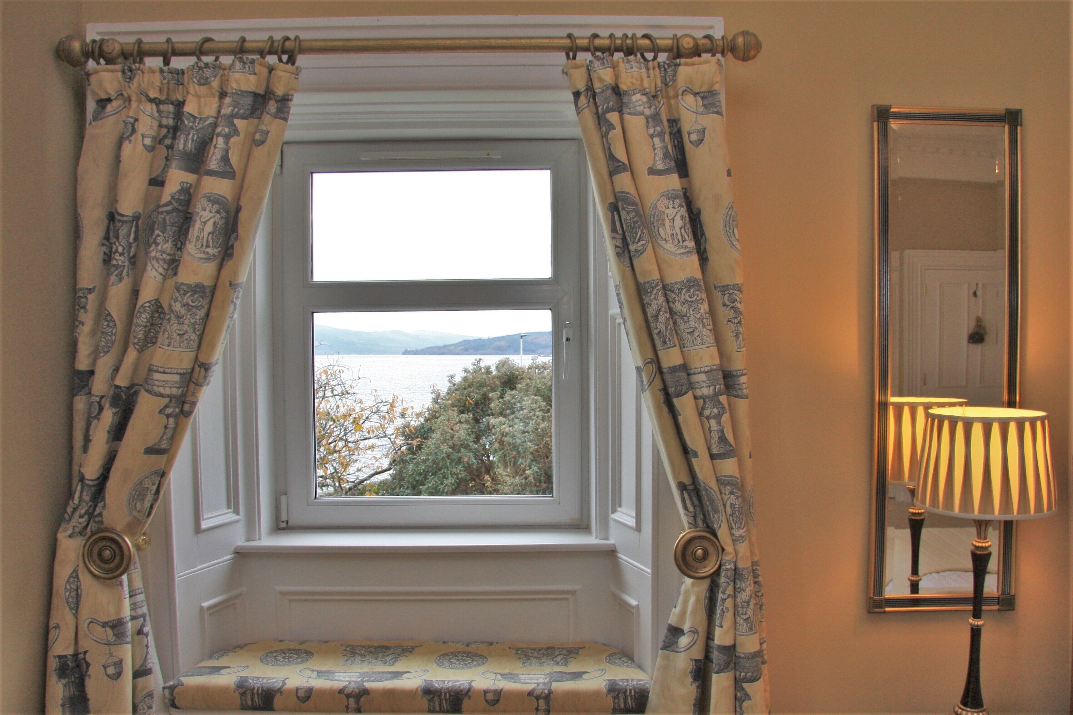 A window with a view of the sea, a bench, and a lamp.