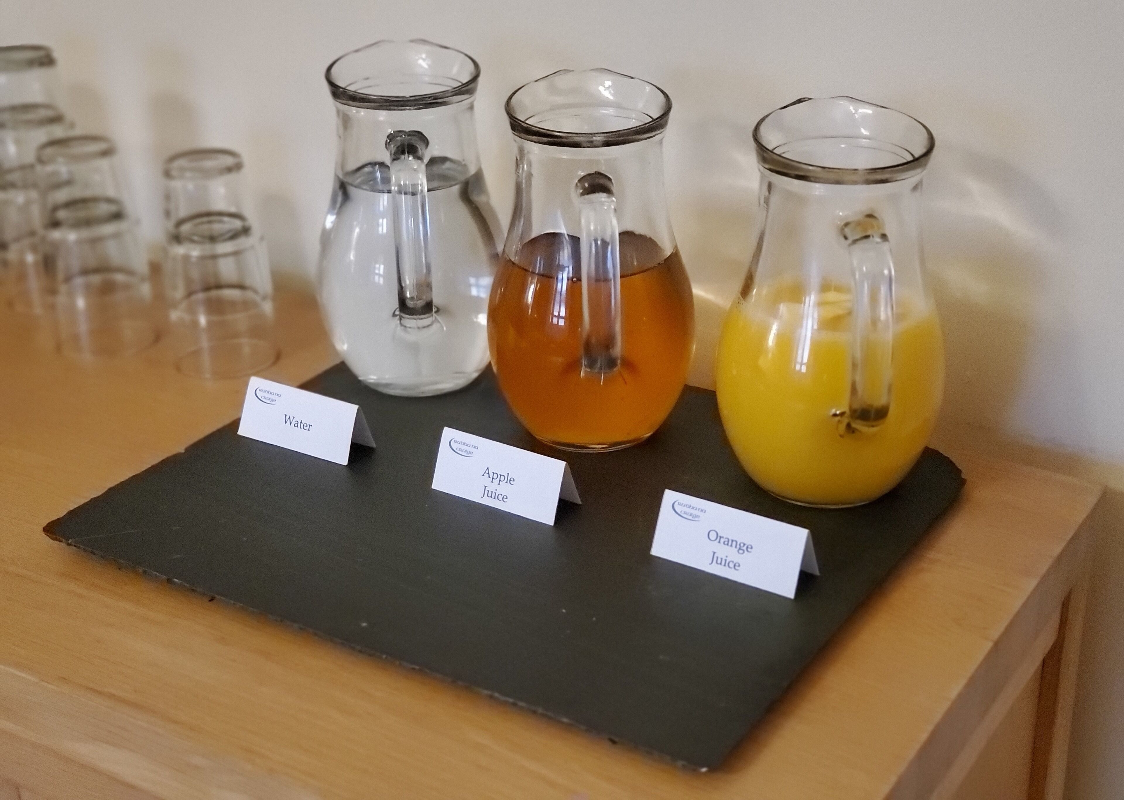 Three glass pitchers labeled with different beverages on a wooden table.
