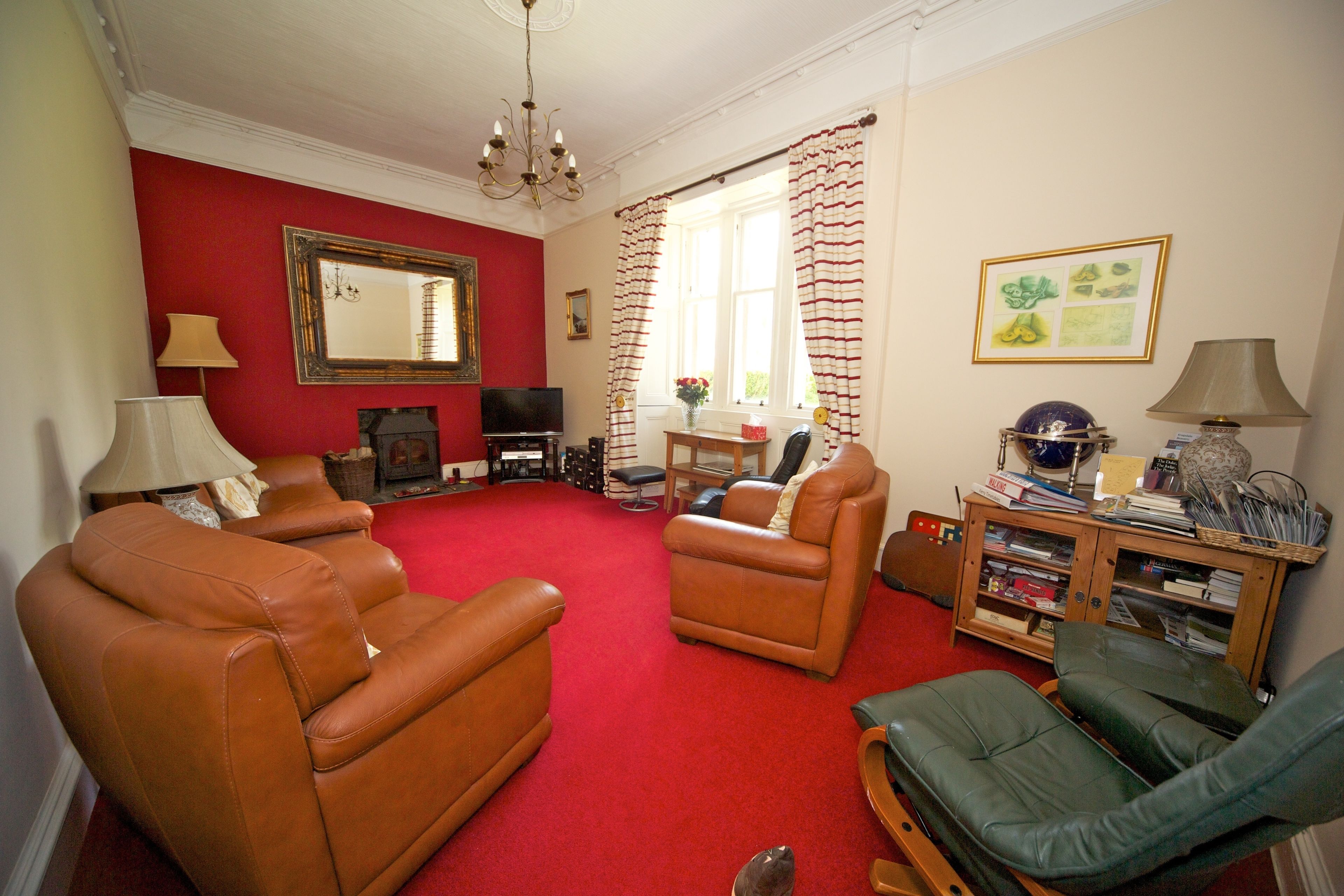 A living room with brown leather sofas, a red carpet, a wooden cabinet with books, a television, and a chandelier.
