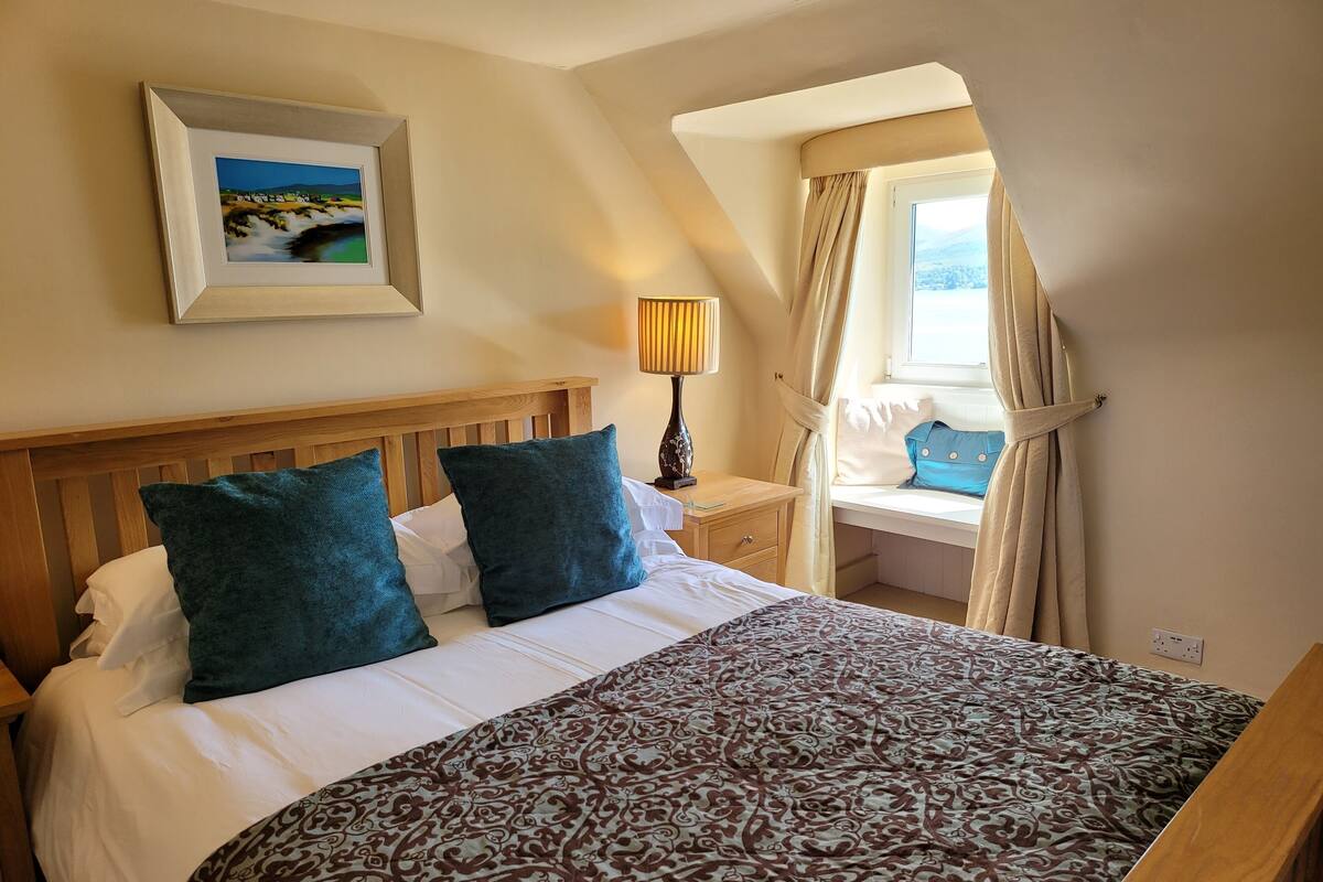 A neatly made bed with a patterned bedspread, a wooden headboard, and two teal pillows.