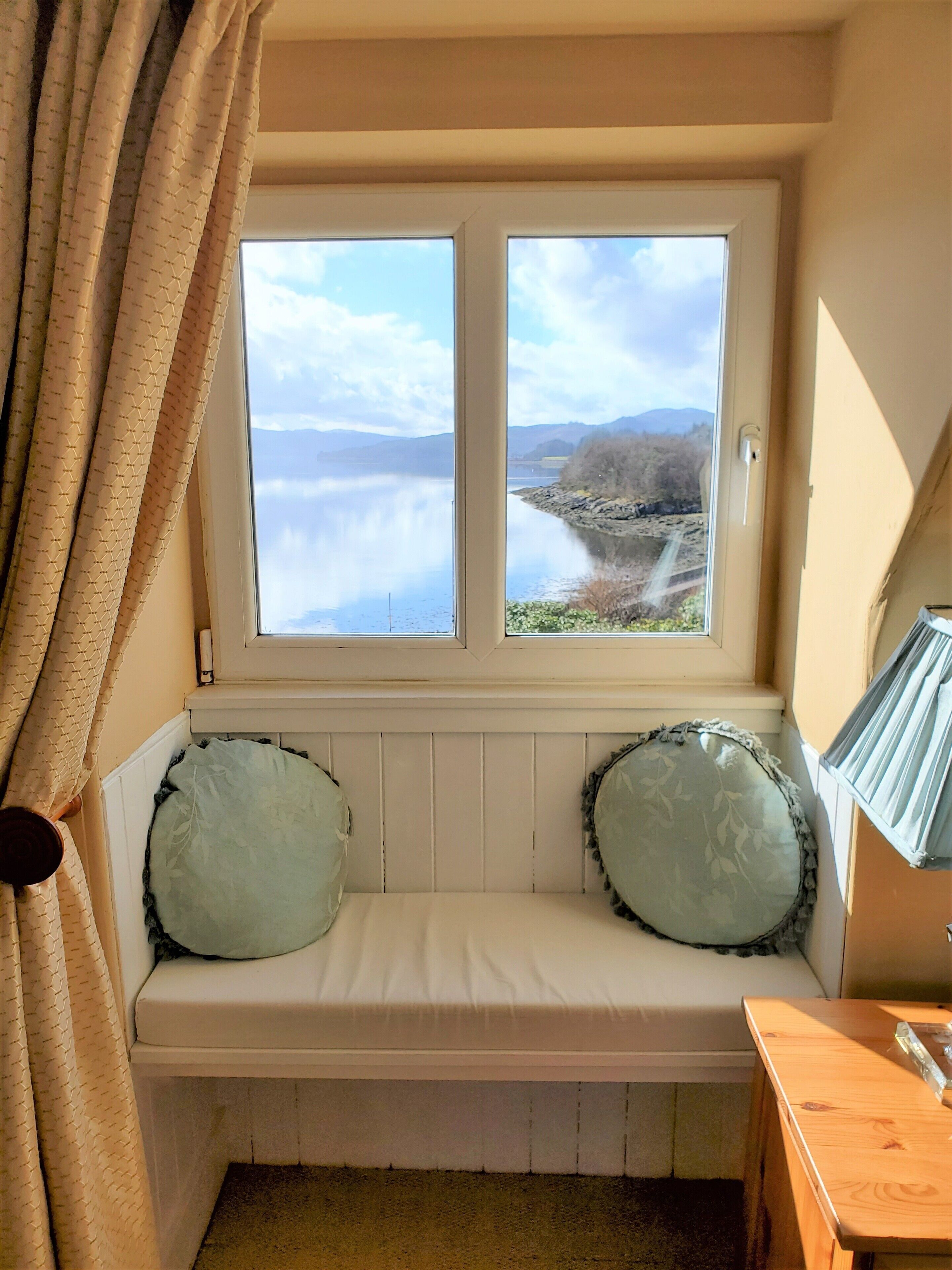 A room with a bench under a window overlooking a lake and mountains.