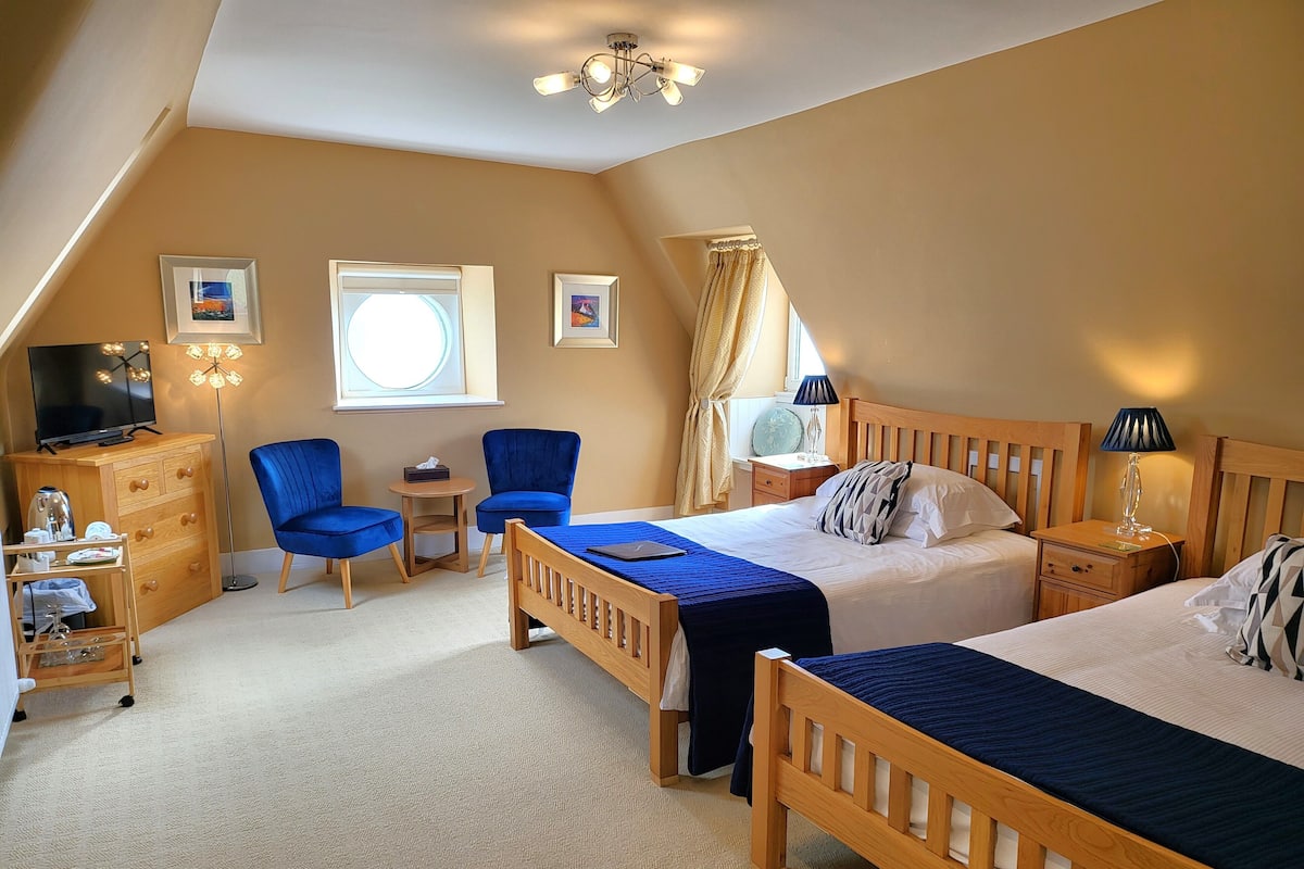 A bedroom with two wooden beds, a TV, a desk, and chairs.