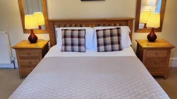 A neatly made bed with a quilted white duvet, flanked by two bedside tables with lamps, a headboard with a mirror, and a framed artwork above the bed.