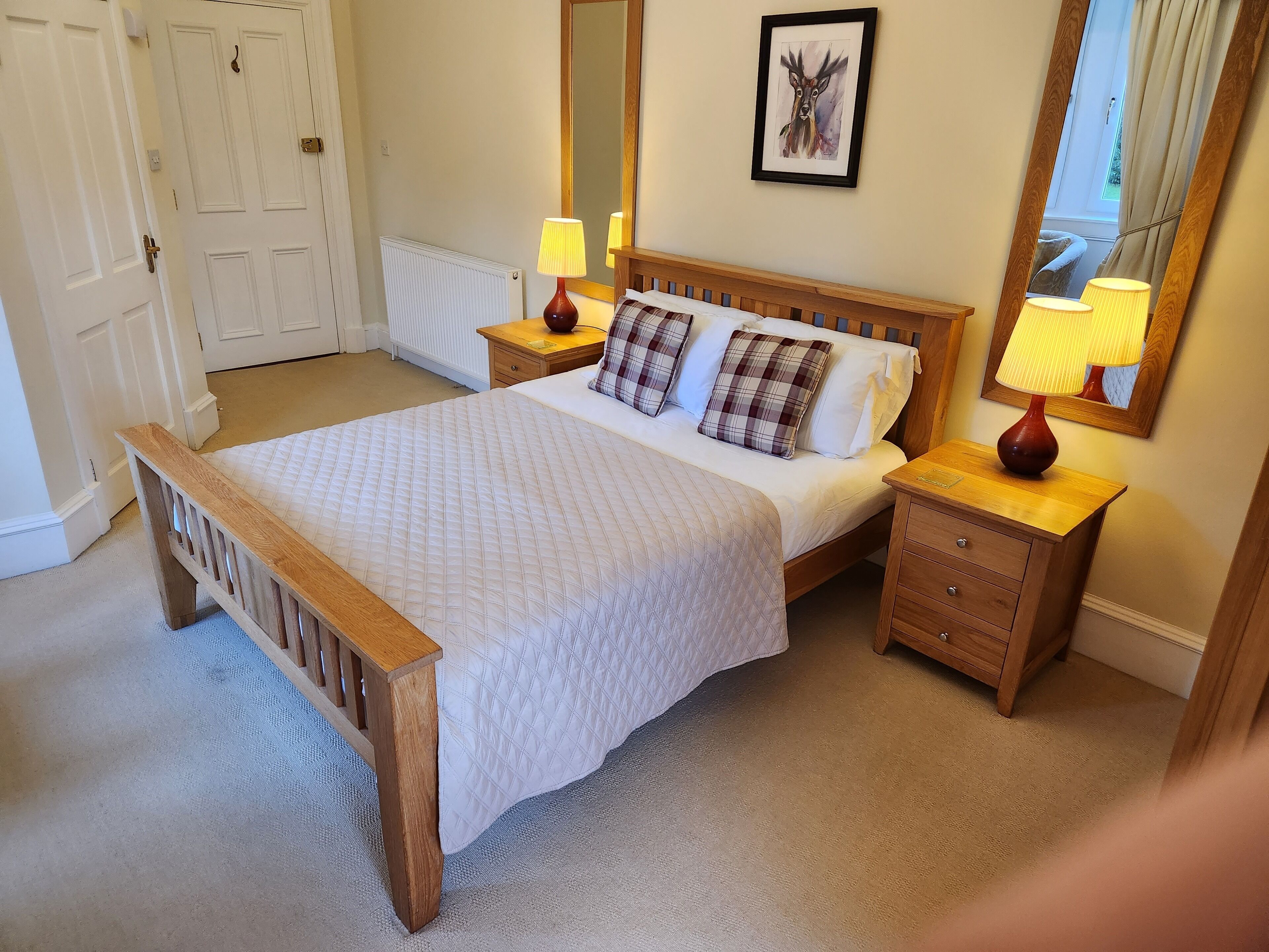A bedroom with a wooden bed, white bedding, two bedside tables with lamps, a large mirror, and a framed picture on the wall.