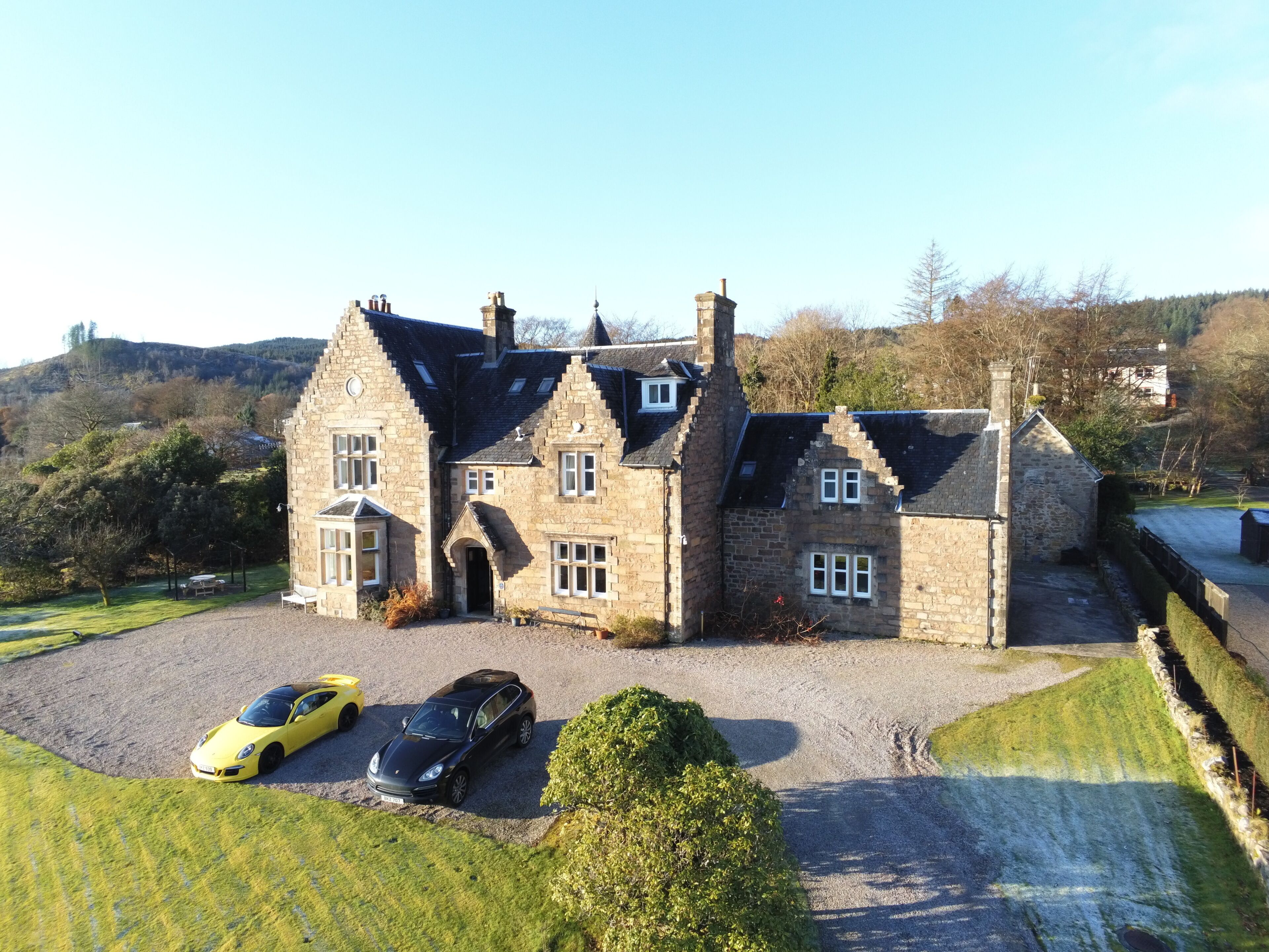 A large stone building with multiple chimneys, a driveway, and two parked cars.