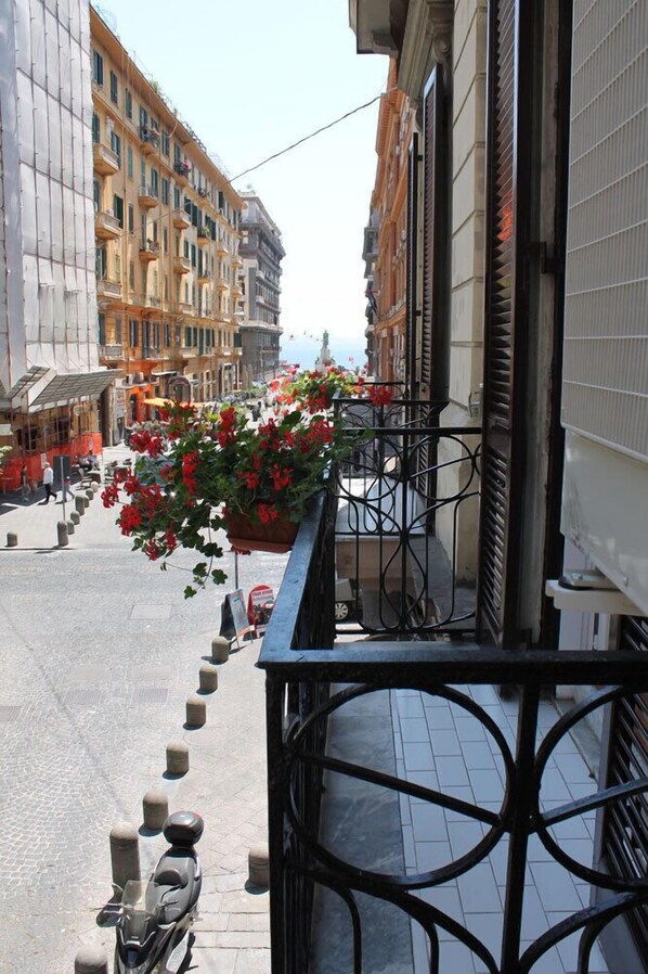 A narrow street with buildings on either side, a scooter parked on the sidewalk, and a flower planter on the balcony. - Le Mummarelle (Naples)