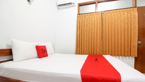 Een net opgemaakt bed met witte lakens, een rode plaid en een kussen, plus een houten hoofdbord.