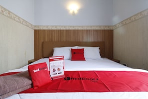 A hotel room with a wooden headboard, white bedding, and red accents including pillows and a blanket. - RedDoorz Plus near Undip Tembalang (Semarang)