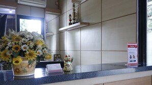 A hotel reception area with a counter, a vase of flowers, a small statue, and a sign on the wall. - RedDoorz Plus near Undip Tembalang (Semarang)