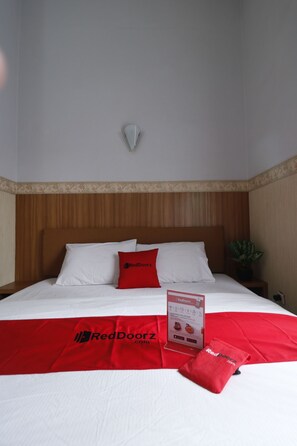 A hotel room with a wooden headboard, white bedding, a red throw blanket, and a RedDoorz sign. - RedDoorz Plus near Undip Tembalang (Semarang)