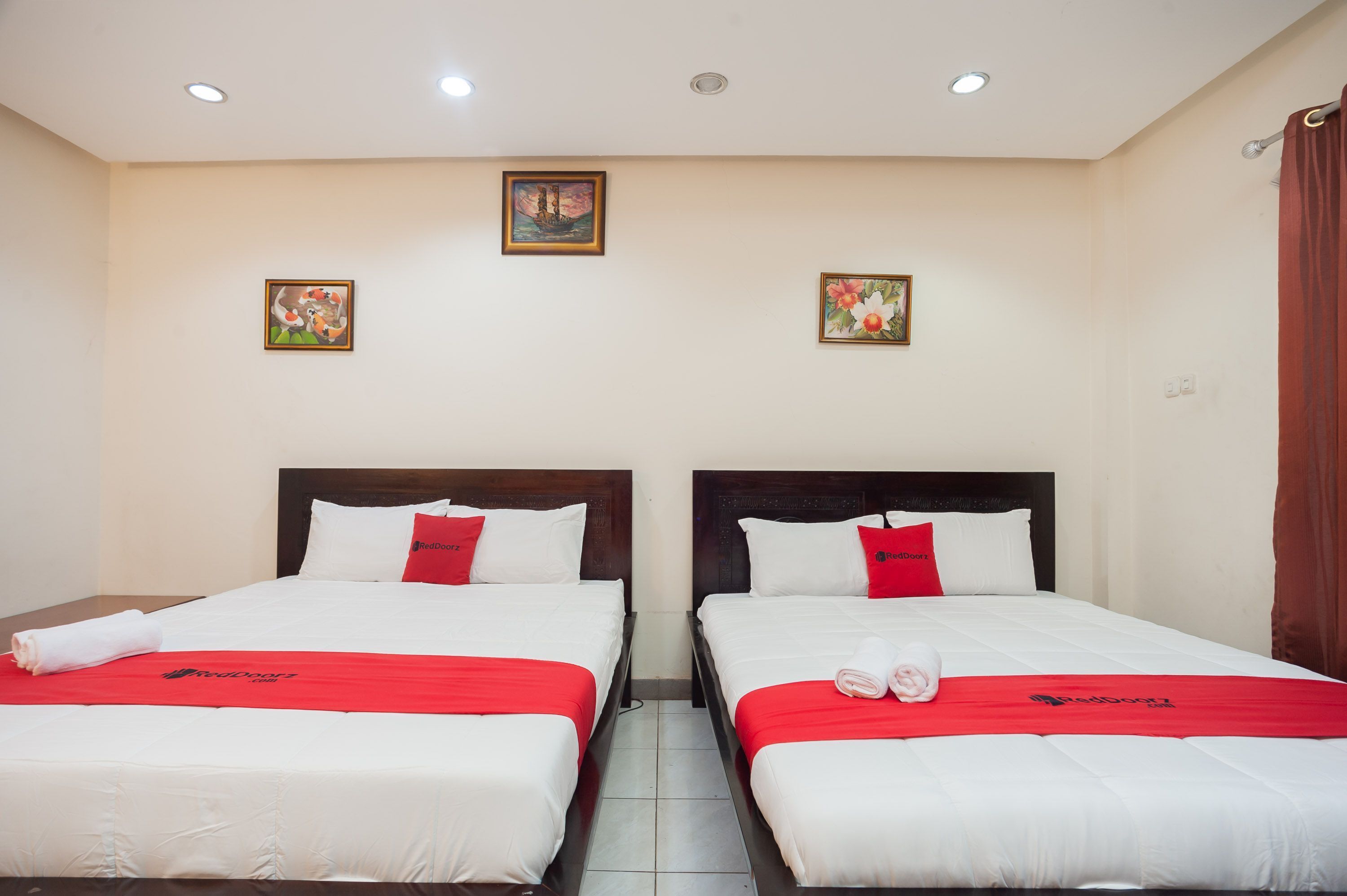 A hotel room with two beds, each with a red blanket and pillows, and a small painting on the wall.