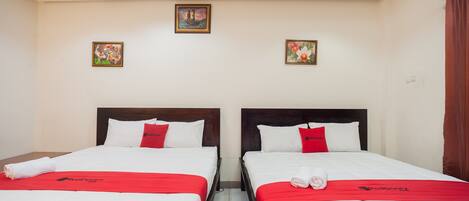A hotel room with two beds, each with a red blanket and pillows, and a small painting on the wall.