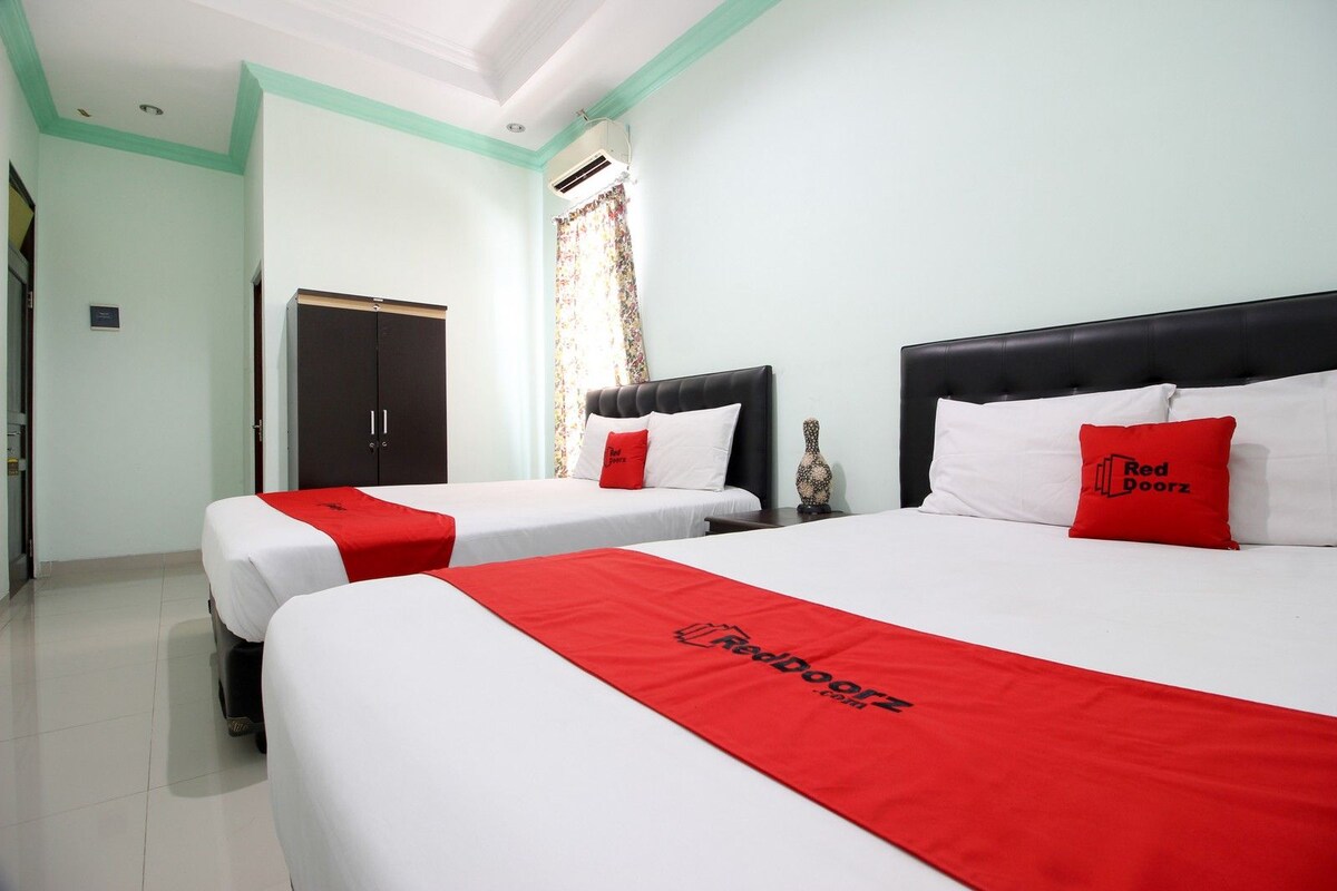 Habitación de hotel con dos camas, cada una con ropa de cama blanca y detalles rojos, cabeceros oscuros y un corredor de cama rojo con el logotipo del hotel.