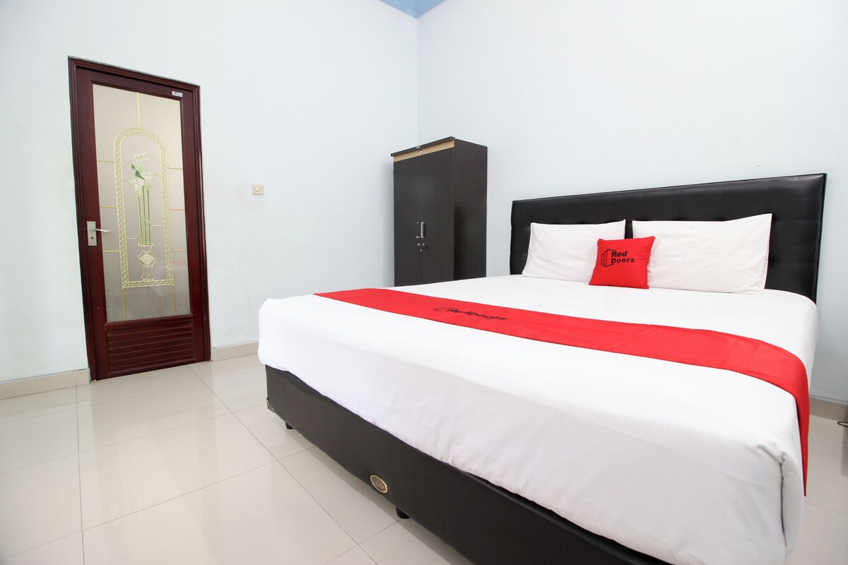 Una habitación de hotel con una cama grande, un armario y una puerta con panel de vidrio decorativo.
